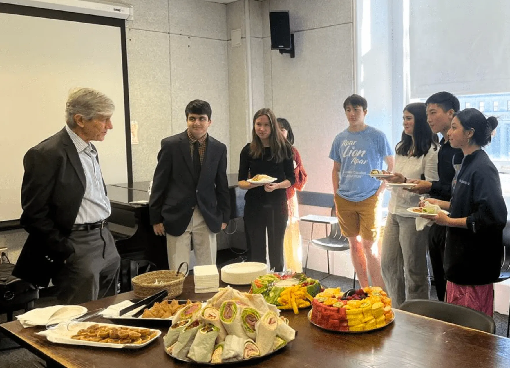 Picture of the recipients of the Rapaport Summer Music Festival Fellowship gathering around a table with food and refreshments. 