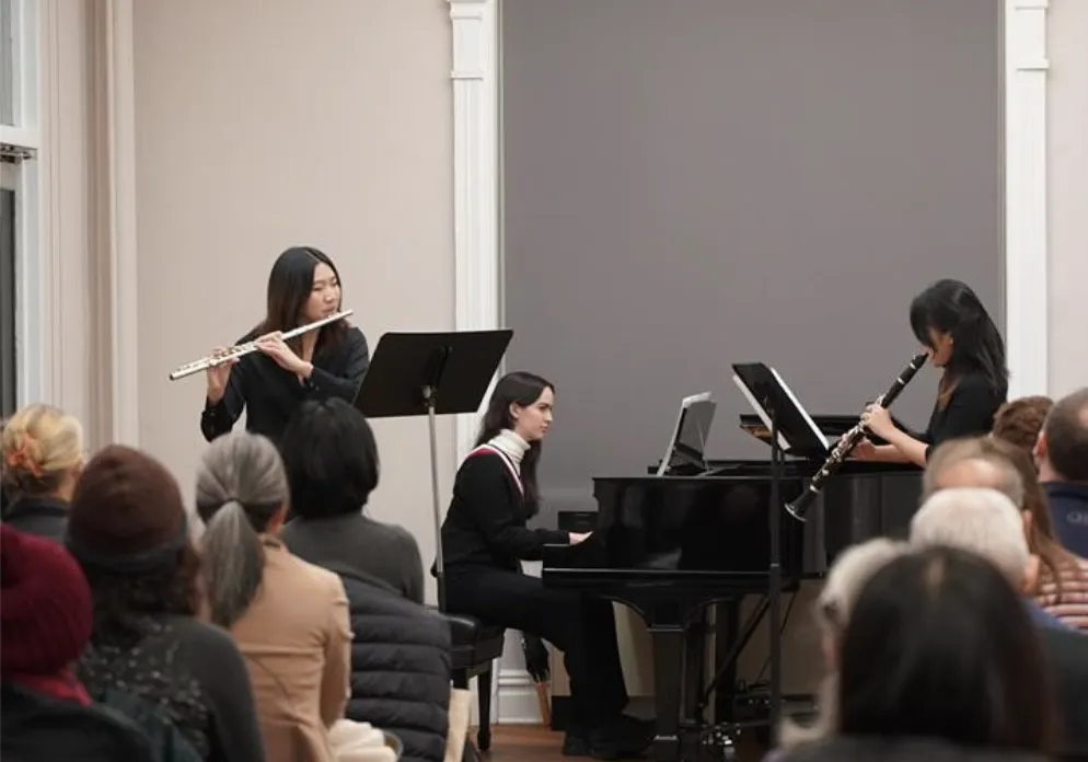 A photo of 3 students: one pianist, one flutist, and one clarinetist performing in the Maison Française.